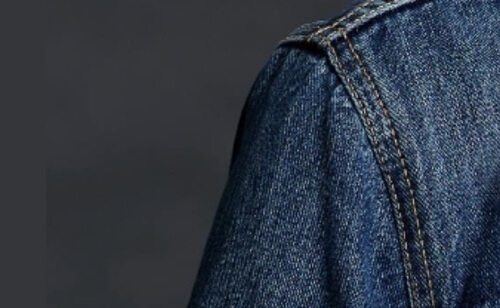 A blue jean jacket with a pocket on the back.